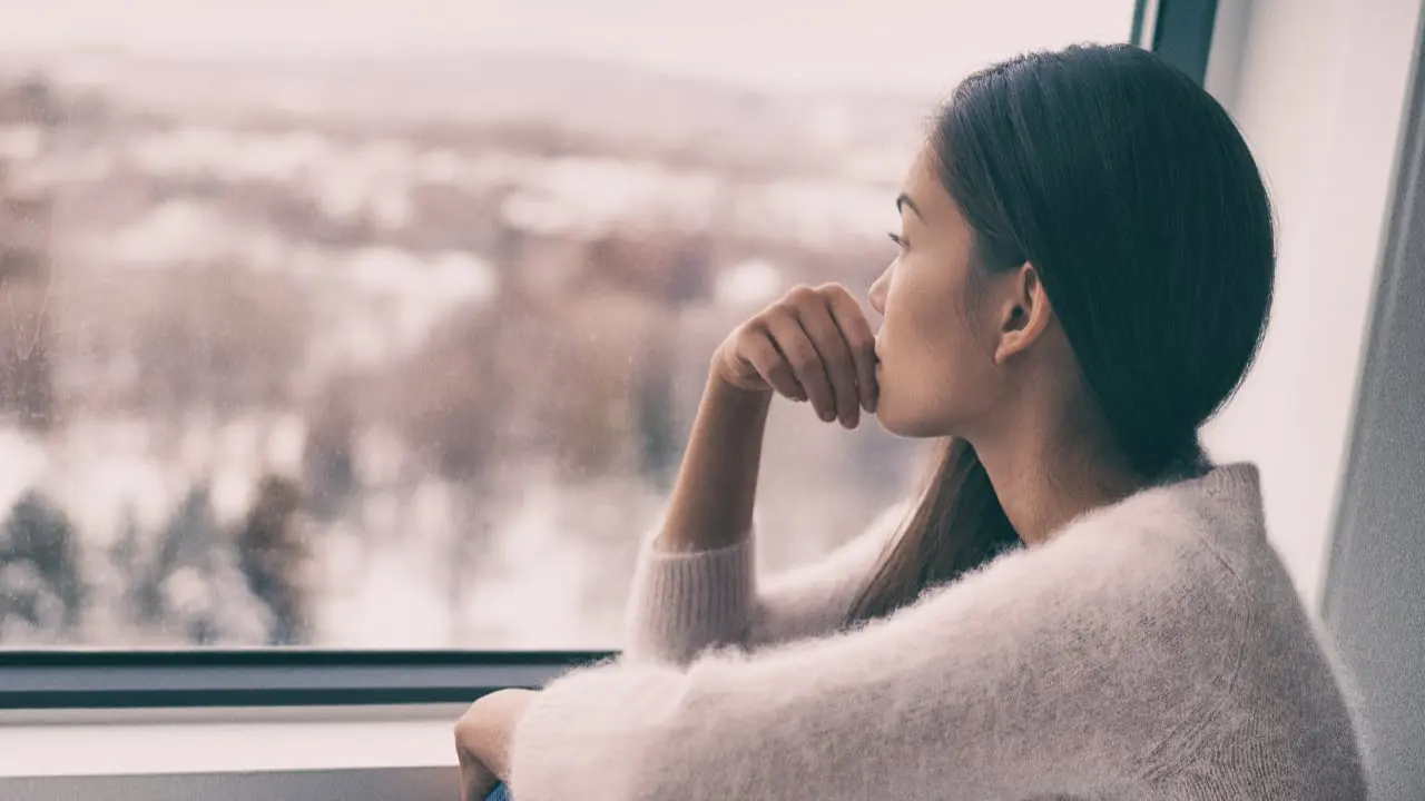 signs-of-depression A thoughtful woman looking out of a window - signs of depression